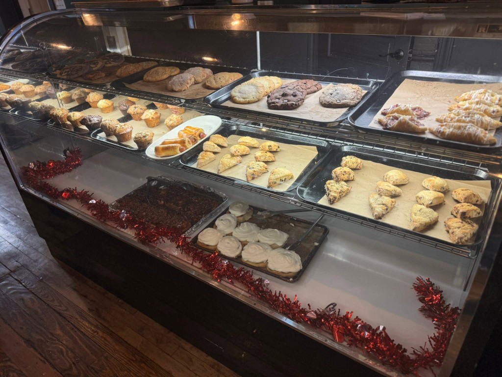 Bakery display case filled with cookies, muffins, scones, and frosted rolls